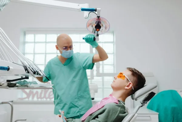 pacient pe scaunul medical si stomatologul langa, cu mana pe lampa