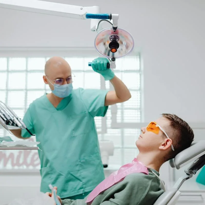 pacient pe scaunul medical si stomatologul langa, cu mana pe lampa